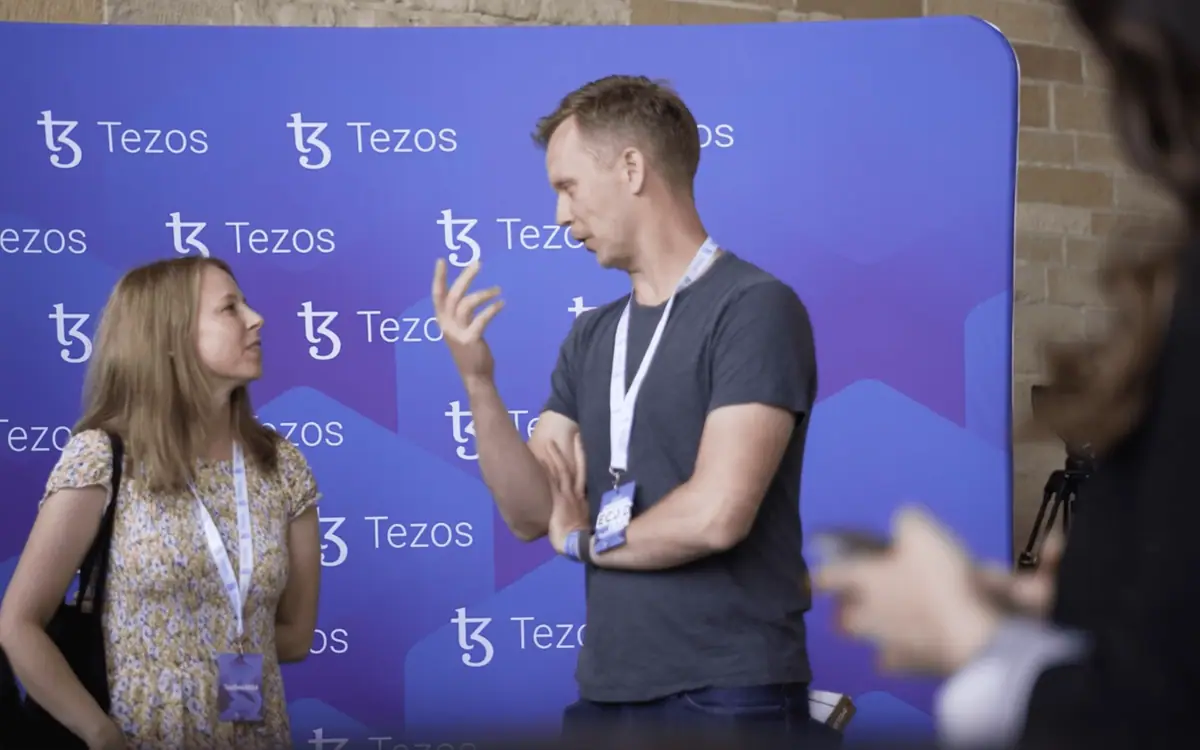 Гости конференции у брендированного press wall Tezos